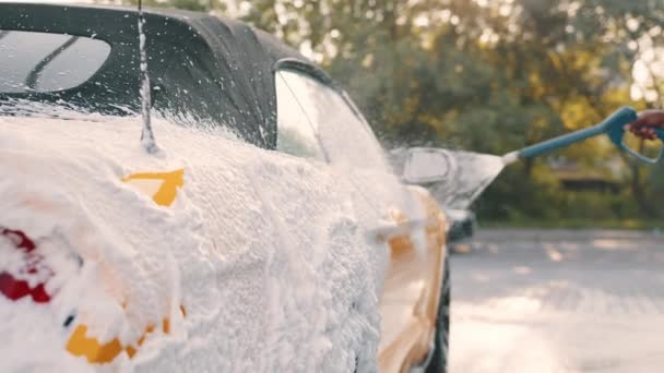 Das Auto ist mit Schaumstoff überzogen. Das Auto wird in einer Waschanlage mit Seife gewaschen. Autowäsche mit Hochdruckreiniger. Waschen im Freien Konzept. Gelbes Auto aus Schaumstoff wird mit Seife gewaschen — Stockvideo