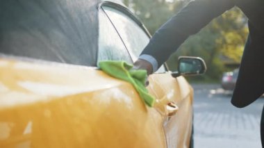 Açık hava self servis istasyonunda oto yıkama ve temizlik. Yakışıklı, sakallı, genç Afrikalı iş adamının resmi fotoğrafı. Yaz güneşli sabahlarda yeşil bir mikrofiber bezle sarı araba temizliği yapıyor..