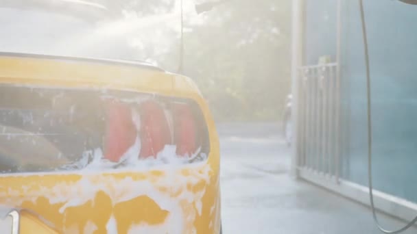 Crop close-up van Afrikaanse knappe jonge zakenman in pak, het schoonmaken van de achterlichten van zijn luxe gele auto met hoge druk water jet bij self car wash service buiten in de zomer ochtend — Stockvideo