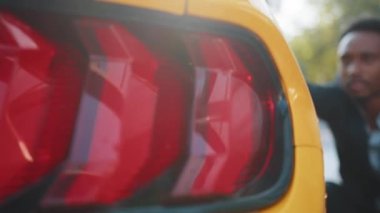 Resmi olarak Afrikalı işadamı dışarıdaki oto yıkama servisinde yeşil mikrofiber bezle araba temizleme farı takıyor. Temiz araba konsepti. Dışarıda araba yıkama.