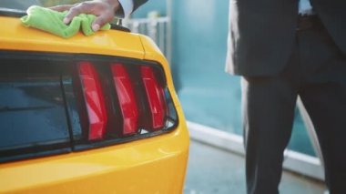 Genç Afrikalı iş adamının el yapımı görüntüsü. Sarı spor arabayı mikrofiber bezle yıkıyor ve temizliyor. Kaputu ve farları siliyor. Araba yıkama konsepti.