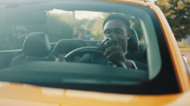 Afro-Amerikan bir iş adamı lüks bir spor arabada oturuyor ve gülümsüyor. Resmi kıyafetiyle arabasını süren yakışıklı, gülümseyen bir Afrikalı 'nın portresi..