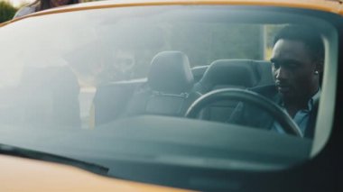 Takım elbiseli Afrikalı bir adam beyaz gömlekli beyaz iş kadınıyla lüks bir arabada oturuyor ve dijital tableti iş için kullanıyor. İki iş ortağı ortak proje hakkında konuşuyor.