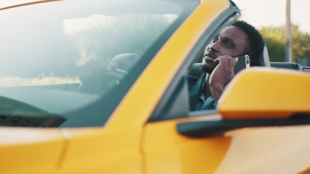 Handsome African American bearded business man in suit, sitting in his modern new car, talking on cellphone, smiling and looking at camera. Happy man owner is testing his new car. — Stock Video