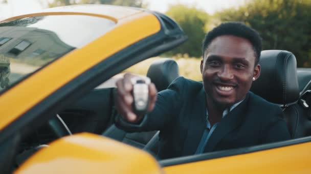 Hombre de negocios afroamericano en traje sentado dentro de su coche deportivo de lujo con llaves en las manos. Hombre guapo se ve satisfecho con la compra exitosa. Concepto de personas, tecnología y transporte — Vídeos de Stock