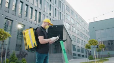Maskeli bir kurye salgın bir dönemde yemek dağıtır. Teslimatçı adam caddedeki akıllı telefon ekranına bakıyor. Karantina sırasında mükemmel atış..