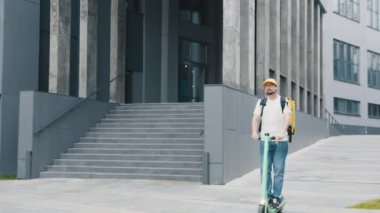 Sarı termal çantalı kurye yemek teslimatı elektrikli scooter teslimatıyla sokakta müşteriye sipariş veriyor. Mükemmel atış. Mal teslimatı ekolojik taşımacılık