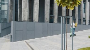 Sırt çantalı ve kaldırımda hızla giden e-scooter 'lı teslimatçı çocuk. Kafelerden ve restoranlardan teslimat servisi. Kurye, elektrikli scooterla yemek getiriyor. Kurye vatandaşlara yiyecek sağlıyor.