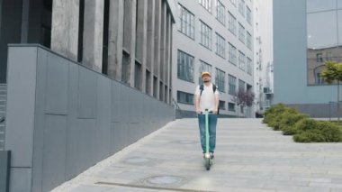 Yiyecek nakliyesi, ulaşım ve insan konsepti. Şehir caddesinde elektrikli scooter kullanan termal yalıtımlı çantalı mutlu bir teslimatçı. Mal teslimatı ekolojik taşımacılık
