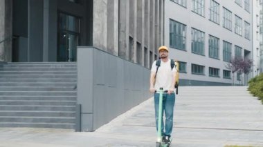 Gülümseyen adam kuryesi sokakta elektrikli scooterla gezen sarı termal sırt çantalı yiyecek getiriyor. Pozitif dağıtım işçisi, çevrimiçi müşteri siparişi teslimatı