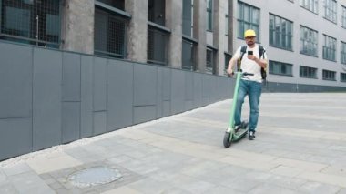 Sırtında büyük bir termal sırt çantasıyla şehirli caddesinde elektrikli scooterla duran müşteriyle akıllı telefondan konuşan erkek kurye yemek teslimatı portresi. Müşteri siparişi. Hızlı teslimat.