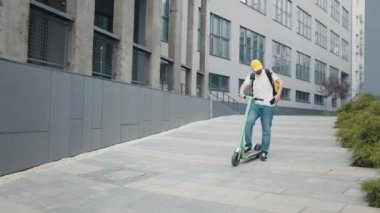 Kafelerden ve restoranlardan teslimat servisi, motosikletli teslimatçı çocuk ve sarı sırt çantası. Kurye e-motosikletle yiyecek getiriyor. Çabuk müşterilere yemek götür. Teslimatçı.