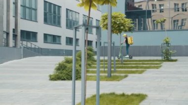 İzotermal sırt çantalı kadın kurye pizza kutusu şehir tarzında elektrikli scooterıyla duvarda geziyor. Kafelerden ve restoranlardan fast food dağıtım hizmeti