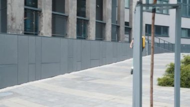 Sırtında sarı bir çanta taşıyan genç bir teslimatçı kız sabahın erken saatlerinde elektrikli scooter kullanıyor. Sarı bir sırt çantası ve sarı bir beyzbol şapkası olan bir teslimat servisinde çalışıyor.