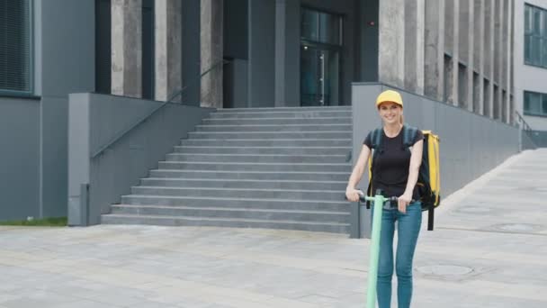 Servizio di consegna donna equitazione scooter nella grande città moderna. Corriere donna con grande zaino termico cavalcando su scooter elettrico in strada guardando altrove. Consegna consegna ordine online al cliente. — Video Stock