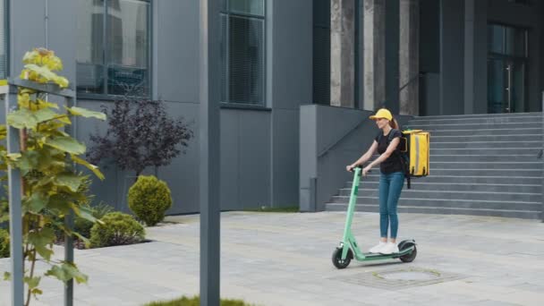 Büyük modern şehirde mobilete binen teslimatçı kadın. Şehir caddesinde elektrikli scooter kullanan termal çantalı bir kadın kurye. Teslimat hizmeti konsepti. Sürdürülebilir taşıma — Stok video