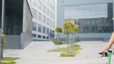 Sarı sırt çantalı bir teslimatçı kadın e-scooter ile video çerçevesine giriyor, etrafa bakıyor, kadın sırtından vuruluyor. Mal teslimatı ekolojik taşımacılık