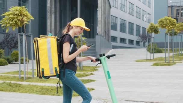 Femme livreur de plats à emporter avec sac à dos isotherme boîte de cas. Gros plan du courrier regarde l'adresse de livraison au téléphone. Femme souriante avec sac à dos thermique regardant smartphone. — Video