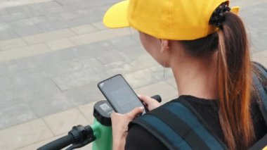 Tanımlanamayan bir kadın sokakta elektrikli scooter kiralamak ve kilidi açmak için QR kodunu akıllı telefonla tarıyor. Şehirde çevre dostu ulaşım. Kapatın. Çevre dostu nakliye aracı. Modern teknolojiler.