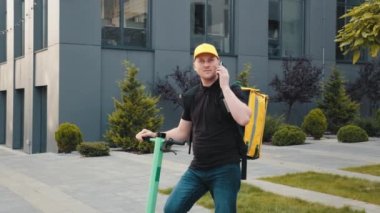 İzotermal yiyecek kutusu olan erkek kurye evin girişine gelir ve müşteri çağırır. Sarı sırt çantalı yemek dağıtım elemanı siparişleri getirdi. Mal teslimatı ekolojik taşımacılık.