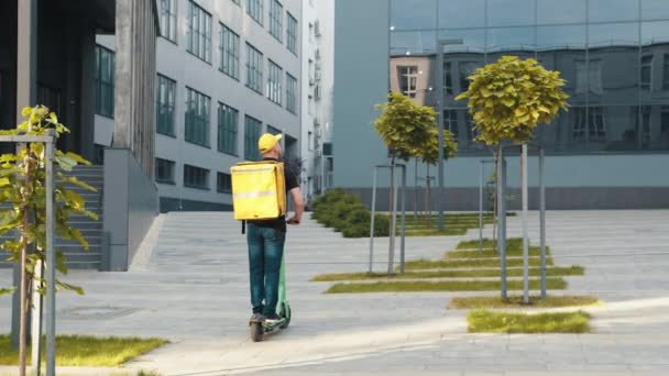 En springpojke med scooter med bagageskrin. Kurir leverera mat med skoter för att undvika trafikstockningar. Snabb och gratis leverans mat med skoter på eftermiddagen i staden — Stockvideo