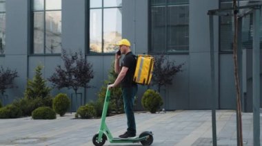 Elektrikli scooter kullanan bir adam telefonda konuşuyor. Elektrikli scooter ve termal sırt çantalı Man Courier yemek teslimatı akıllı telefon kullanarak müşteri siparişini onayla.