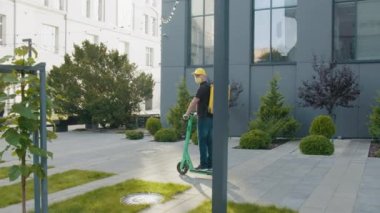 Teslimatçı koruyucu maske takıyor ve modern evlerin ya da büroların önüne mobiletli çanta, ekspres yemek teslimatı ve online alışveriş konseptiyle yiyecek paketi göndermeye hazır..