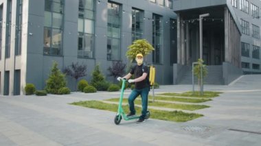 Yakışıklı, koruyucu steril tıbbi maskeli, sırt çantalı, modern elektrikli scooter kullanan genç bir adam. Coronavirus, virüs, epidemik covid-19, ekolojik taşıma konsepti. Karantina sırasında teslimat