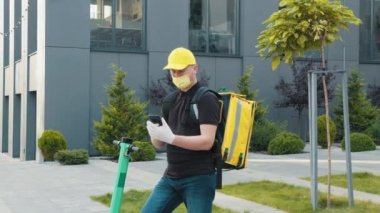 Maskeli kurye şehir caddesinde cep telefonuyla arama yapıyor. Dışarıya yemek götürmek için akıllı telefonu kullanan bisikletli kurye. Teslimat hizmeti ve küçük işletme konsepti.