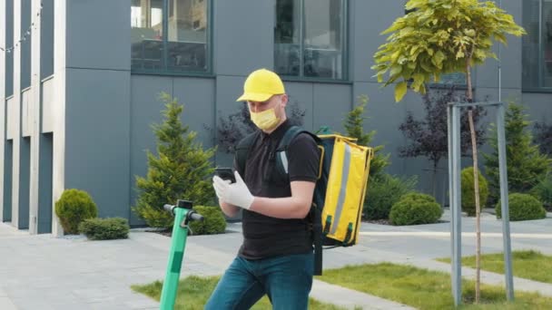 Entrega homem em máscara procurando endereço com telefone celular na rua da cidade. Correio de bicicleta usando smartphone para entregar comida ao ar livre. Serviço de entrega e conceito de pequenas empresas. — Vídeo de Stock