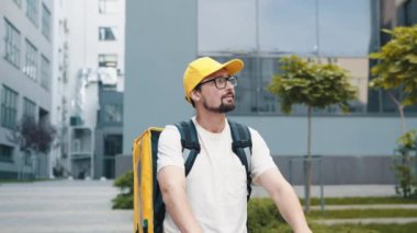 Şehrin caddesinde yalıtılmış bir çantayla poz verirken kameraya bakan genç bir yemek kuryesinin portresi. Müşteri evine ya da ofisine fast food getiren neşeli kurye. Konsept Teslimat