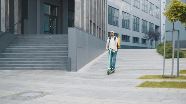 Los mensajeros realizan pedidos para la entrega de mercancías. Hombre mensajero en scooter entrega de alimentos en las calles de la ciudad con una entrega de comida caliente de comida para llevar y restaurantes a casa. Entrega de comida por scooter — Vídeos de Stock