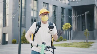 Bisikletli kurye, akıllı telefon kullanarak müşteriyle konuşuyor, yiyecek getiriyor. Teslimat servisi ve küçük işletme konsepti. Maskeli bir satıcı şehirdeki bir cep telefonundan adres arıyor..