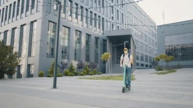 Yemek teslimatı. Kurye Adam Restoran Yemekleri Kutuda, E-Motosikletli açık havada poz veriyor. Yiyecek kutusu olan kurye elektrikli scooterla geliyor. Elinde telefon olan bir kurye.
