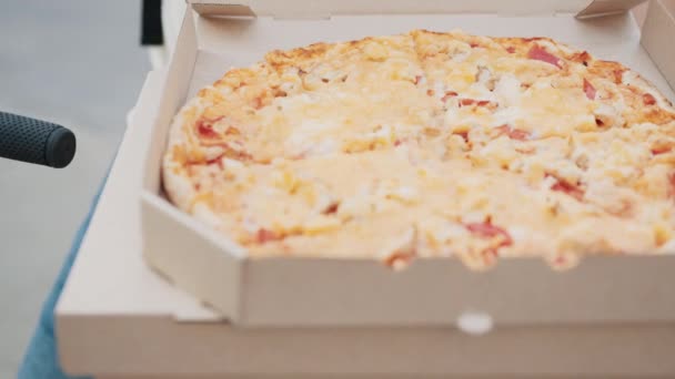 箱の中のピザのクローズアップ。サラミとチーズのピザ。食べ物の概念。オープンボックスからのホットおいしいイタリアのピザ、パーティーケータリングのコンセプトでの食品配達サービス。手がピザボックスを開く. — ストック動画