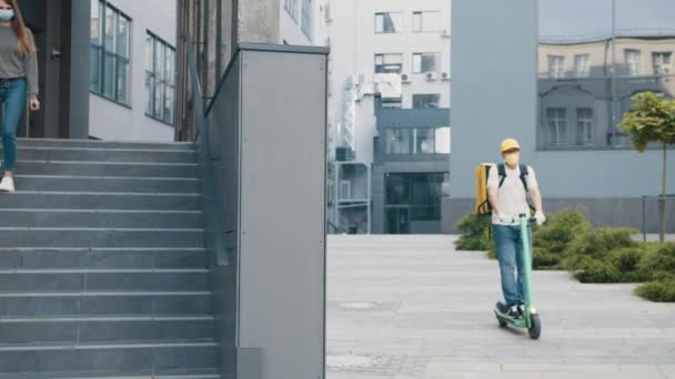 Servicio de mensajería. Chica recoge la caja de entrega del conductor de entrega con scooter Cerca de una gran oficina o edificio en la ciudad. Mujer joven se encuentra con el hombre de entrega que le da su caja de cartón paquete postal — Vídeos de Stock