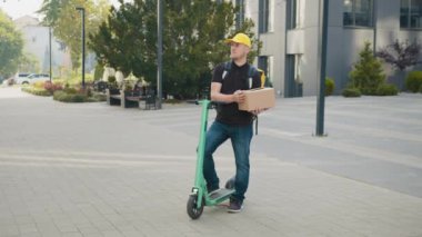 Scooter teslimatı, hızlı teslimat ve online alışveriş konsepti yapan bir kurye. Teslimatçı E-motosiklet servisi, Hızlı ve Ücretsiz Ulaşım. Karton kutu taşıyan teslimatçı.