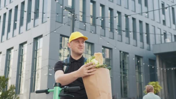 Delivery Concept - Handsome delivery man carrying package box of grocery food and drink from store. Close up on sunlight courier in uniform holding package with food. Door-to-door food delivery worker — Stock Video