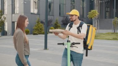 Pizza teslimatı. Kız pizza siparişi verdi. Yakışıklı teslimatçı çocuk elinde sıcak pizzayla kutular tutuyor. Arkadaş canlısı teslimatçı müşteriye pizza veriyor.