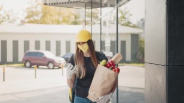 Üniformalı, şapkalı, tıbbi maskeli, eldivenli genç teslimatçı kadın. Taze bakkal torbası taşıyan, telefon dinleyen ya da dışarıda kayan. Cep telefonundan adres arayan bir satıcı.