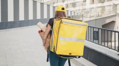 Sarı şapkalı ve tişörtlü güzel beyaz bir kadın güneşli bir günde sokakta yürüyor ve yanında yemek paketi taşıyor. Elinde market poşeti olan bir kadın kurye teslim ediyor. Teslimat alışverişi