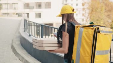 Elinde telefon olan beyaz, genç bir kadın kurye. Kurye 'nin arkasından termal torba ve pizza kutusuyla ateş etmek. Kurye telefona bakar ve caddede yürür.