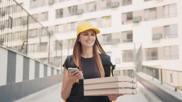 스마트폰을 이용하여 도시에서 맛있는 피자를 배달하는 유쾌 한 여성. 행복 한 여성 택배 원 이 피자 배달 일을 하고 있습니다. 식량 공급의 개념입니다. 온라인 쇼핑 — 비디오