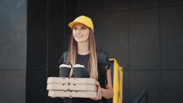 Vrouw geeft een fast food order op de achtergrond van een modern gebouw in de buurt van het huis. Een koerier met een papieren zak met eten, koffie of pizza. Thuisbezorging van producten uit een winkel of restaurant. — Stockvideo