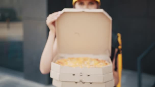 Pizza delivery service. Delivery woman is showing the pizza. Happy young woman holding hot pizza in box. Female worker of food delivery service near house outdoors. — Stock Video