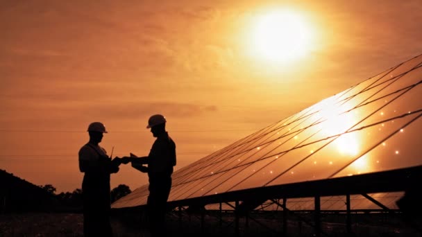 两名身份不明的太阳能工程师在夕阳西下背光下。太阳能公园。替代能源概念。接收光子生态可再生能源电站能源薄膜太阳能技术电 — 图库视频影像