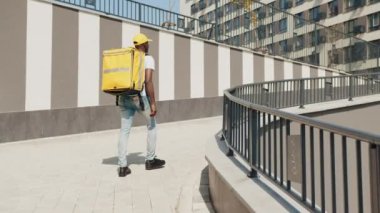 Yakışıklı Afro-Amerikan kurye, teslimat işçisi, kep ve sağlık maskesi yolda yürürken bir paket taze yiyecek taşıyor. Genç bir kurye yiyecek getirecek. Teslimat konsepti