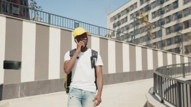 Genç bir Afro-Amerikalı teslimatçı elinde sarı bir termal çantayla şehir caddesinde yürüyor ve telefonla konuşuyor. Müze müdürü siparişi vermek için acele ediyor. Teslimat servisi, eve veya ofise sipariş verin.