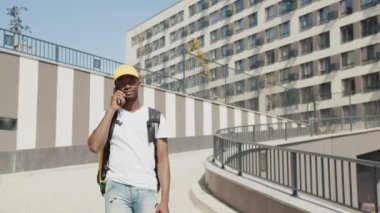 Elinde yiyecek torbası olan Afro-Amerikalı bir kurye elinde telefonuyla sokakta yürüyüp cep telefonundaki adresi arıyor. Teslimat servisi, eve veya ofise sipariş verin.