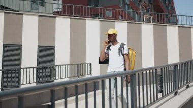 Genç bir Afrikalı kurye termal sırt çantasıyla bir şehir caddesinde yürüyor, bir restoran veya dükkandan sipariş getiriyor. Kurye telefonda konuşur ve emirleri uygular. Çeşitli malların hızlı teslimi